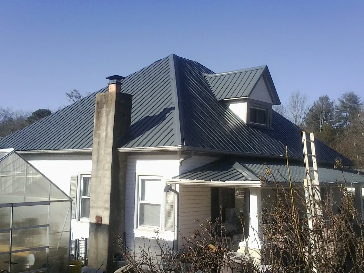 Dark blue standing seam metal roof on a white farmhouse with dormer — Slate & Tile Roof Repair by Roofing Brothers in Boyds