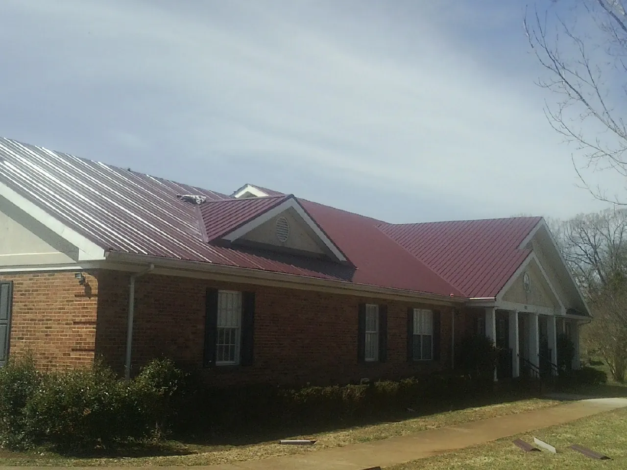 Red metal roof with gabled entries on a long brick building, from a Hail Damage Roof Repair job in Boyds