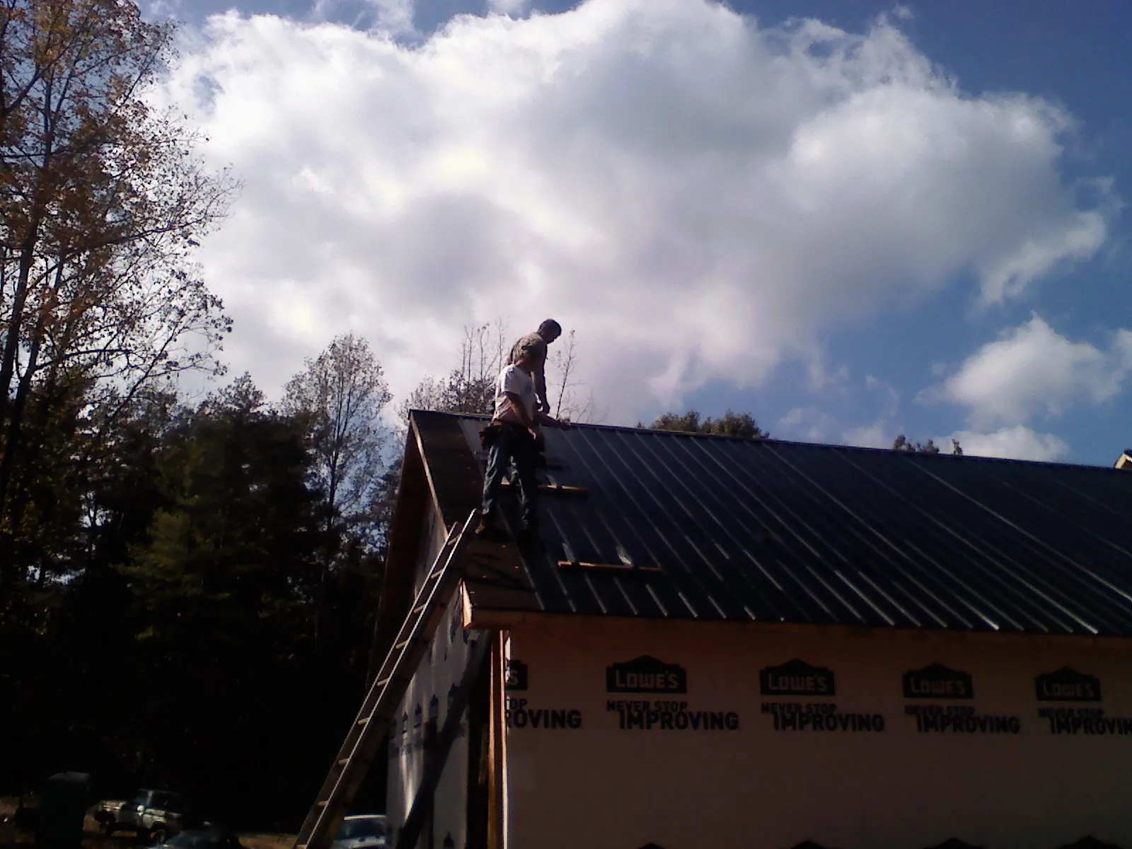 Roofer fastening dark metal panels high against a cloudy sky, from a Roof Inspection job in Boyds